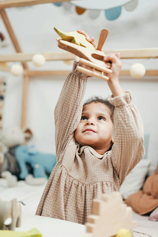 a little girl holding a toy airplane above her head, inspired by The Family Circus, renaissance, neutral colours, sustainable materials, activity play centre, vanilla