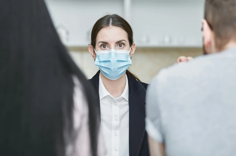 a woman wearing a face mask in a group of people, a picture, trending on pexels, hurufiyya, local conspirologist, someone lost job, conservatively dressed, looking from shoulder