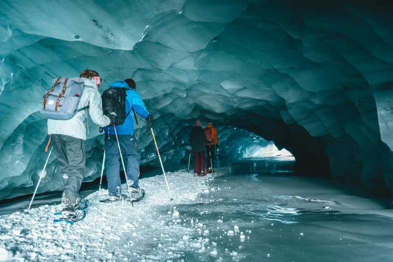 a group of people riding skis down a snow covered slope, cavern ceiling visible, ice blue, walking, lpoty