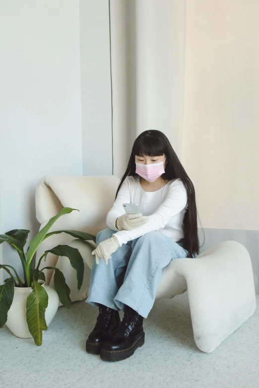 a woman sitting in a chair wearing a face mask, by helen huang, trending on pexels, aestheticism, ulzzang, white and pink cloth, teenager, waiting room