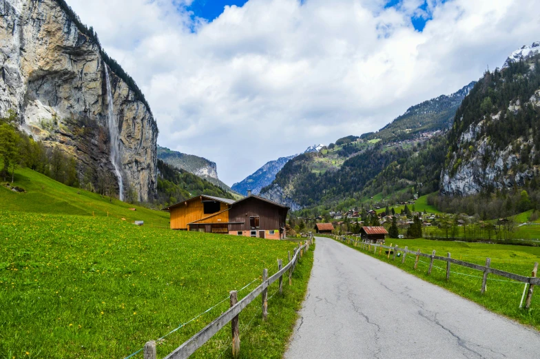 a road going through a lush green valley, a picture, by Julia Pishtar, lauterbrunnen valley, wooden houses, conde nast traveler photo, abcdefghijklmnopqrstuvwxyz