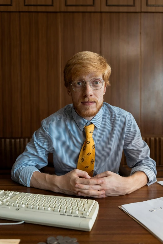 a man sitting at a desk in front of a computer, an album cover, by Andrew Stevovich, ginger hair with freckles, dress shirt and tie, librarian, 2019 trending photo