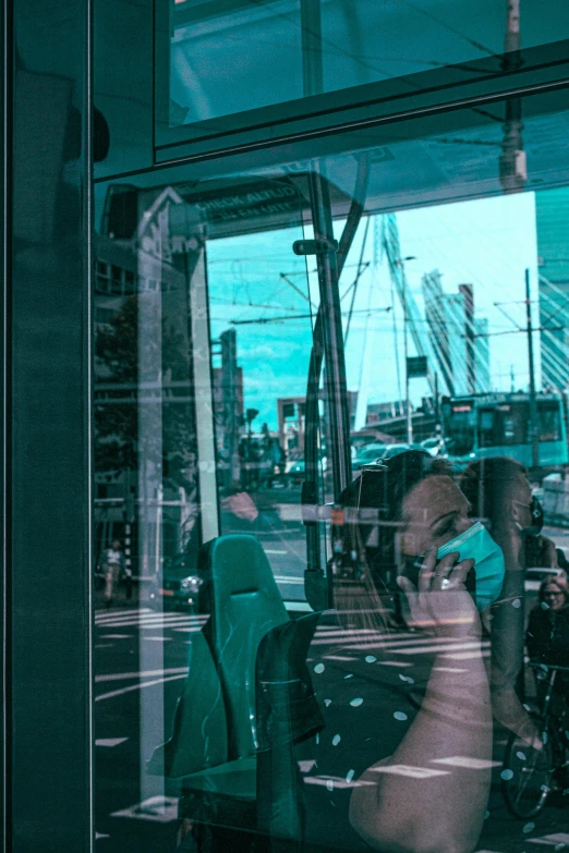 a man sitting on a bus talking on a cell phone, a picture, by Niko Henrichon, pexels contest winner, city reflection, black and cyan color scheme, shop front, inside large window of ship