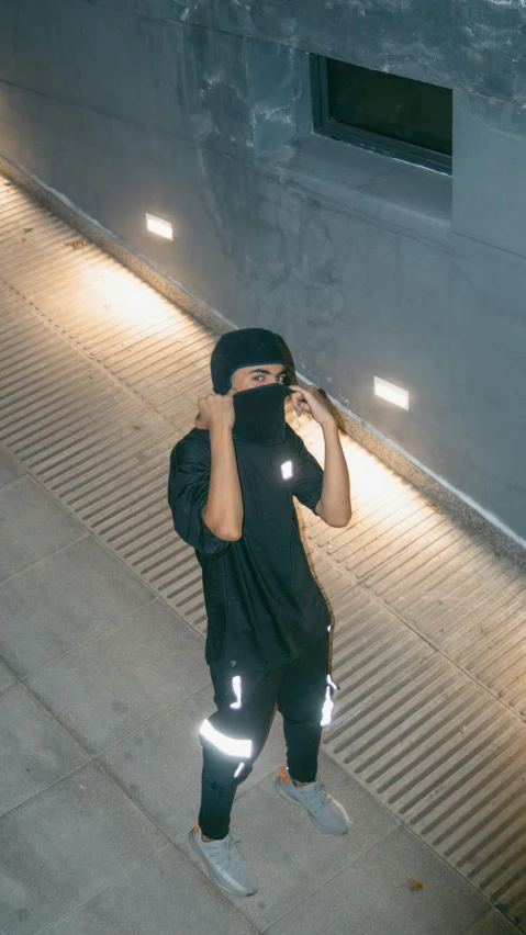 a person standing on a sidewalk talking on a cell phone, an album cover, inspired by Zhu Da, unsplash contest winner, hurufiyya, dark visor covering top of face, black jersey, 15081959 21121991 01012000 4k, sport clothing