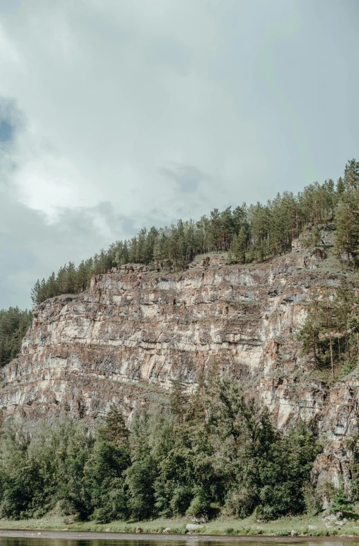 a body of water with a mountain in the background, on a cliff, pine forests, geological strata, paul barson