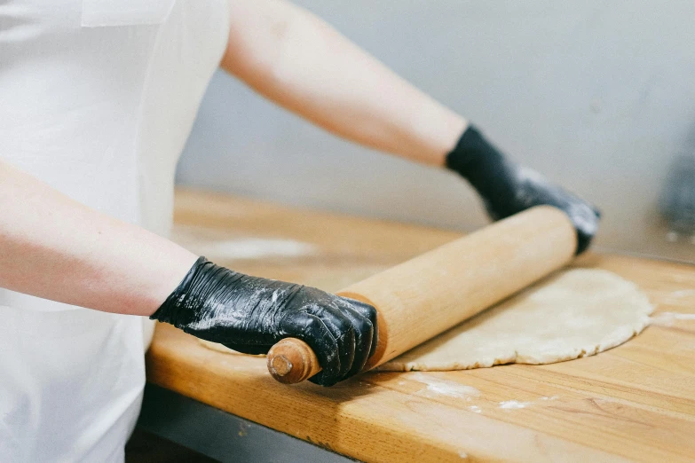 a person rolling out dough on a wooden table, a portrait, by Julia Pishtar, trending on pexels, white long gloves, black bandage on arms, bakery, mechanised