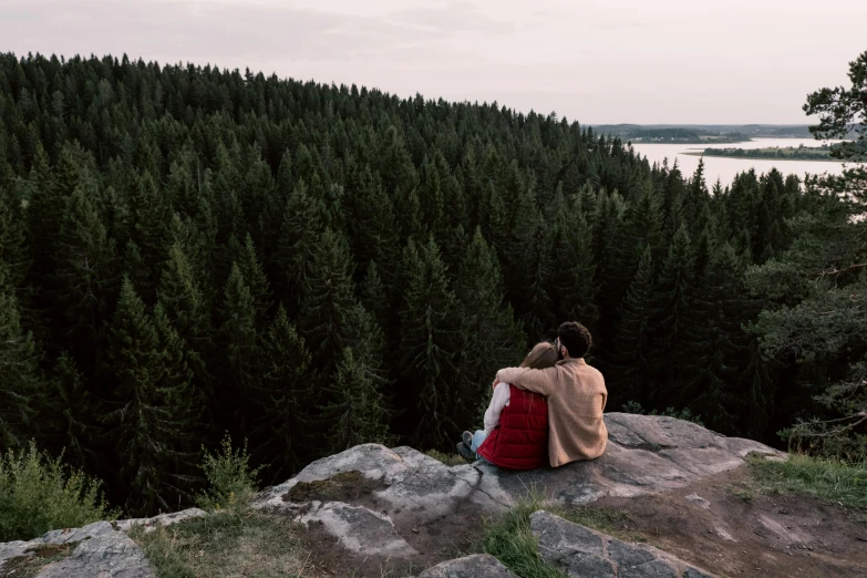 a couple of people sitting on top of a rock, by Jaakko Mattila, pexels contest winner, evergreen forest, view from back, shot on hasselblad, panoramic view of girl