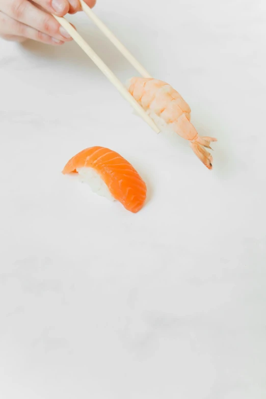 a person holding chopsticks over a piece of sushi, inspired by Koson Ohara, unsplash, sōsaku hanga, prawn, minimalist photo, made of glazed, fish tail