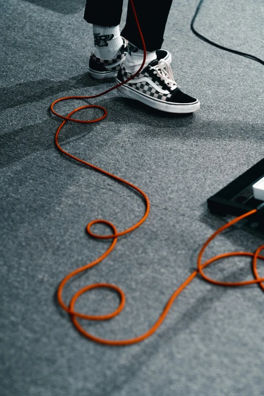 a person that is standing in front of a keyboard, cables on floor, orange and black, thick looping wires, shoes