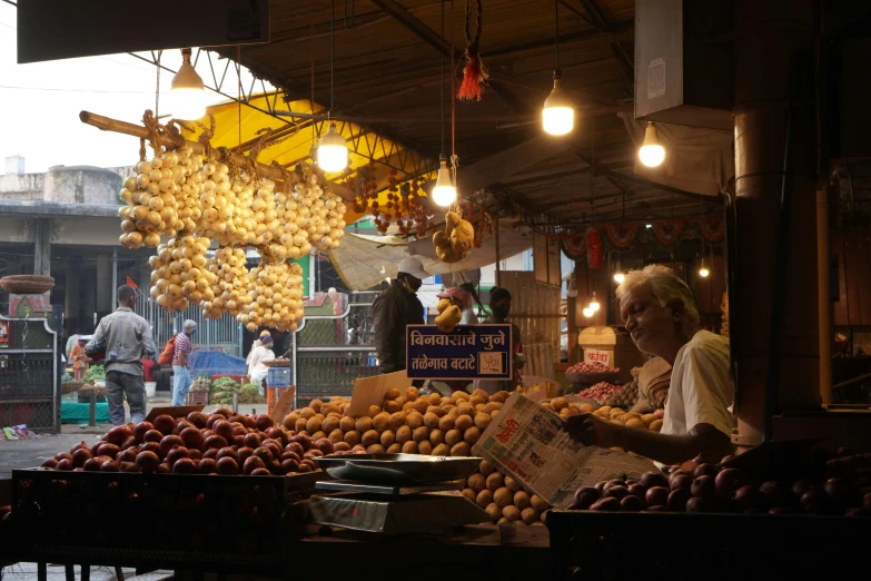 a man standing in front of a fruit stand, unsplash, samikshavad, lights on, square, potato, ritu kumar