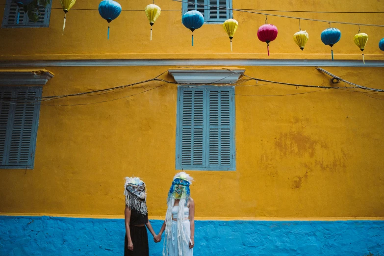 a couple of people that are standing in front of a building, inspired by Steve McCurry, unsplash contest winner, yellow and blue and cyan, vietnamese woman, wearing an elaborate helmet, avatar image