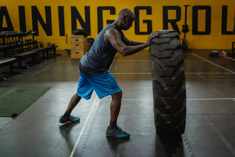 a man lifting a large tire in a gym, a portrait, by Robbie Trevino, dribble, profile image, turning yellow, johnson ting, mc ride