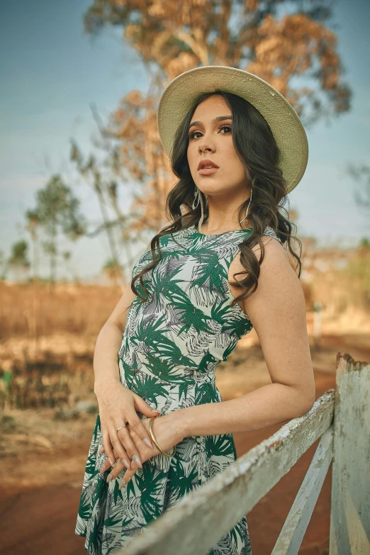 a woman in a dress and hat leaning on a fence, an album cover, by Alejandro Obregón, pregnant belly, promo image, trees, close up half body shot
