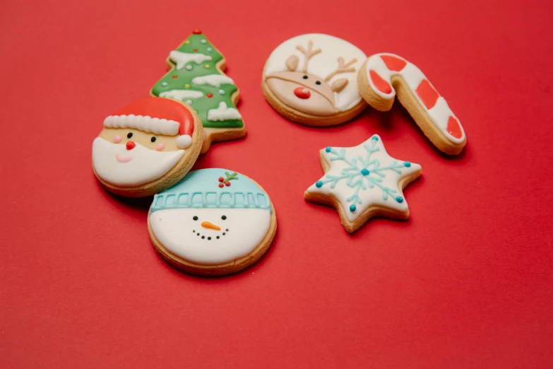 a number of decorated cookies on a red surface, a picture, by Paul Bird, pexels, full face shot, official product photo, frosty, various posed