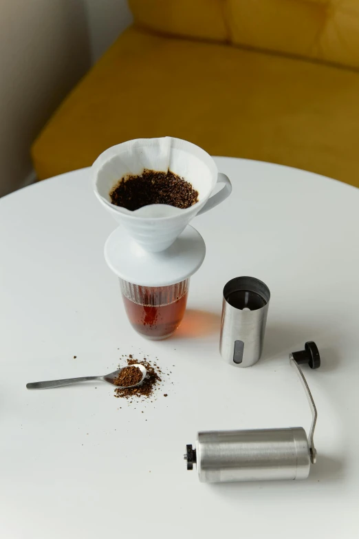 a coffee maker sitting on top of a white table, next to a cup, thumbnail, botanicals, kano)