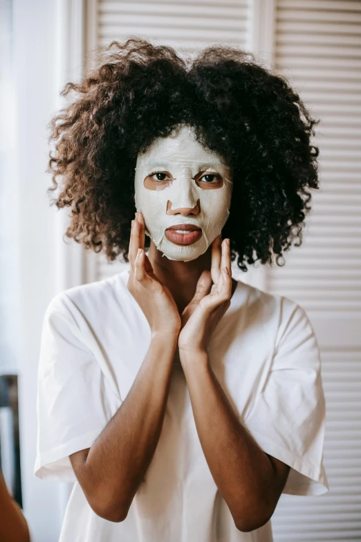 a woman with a face mask in front of a mirror, trending on pexels, brown skin like soil, eucalyptus, with textured hair and skin, robe. perfect faces