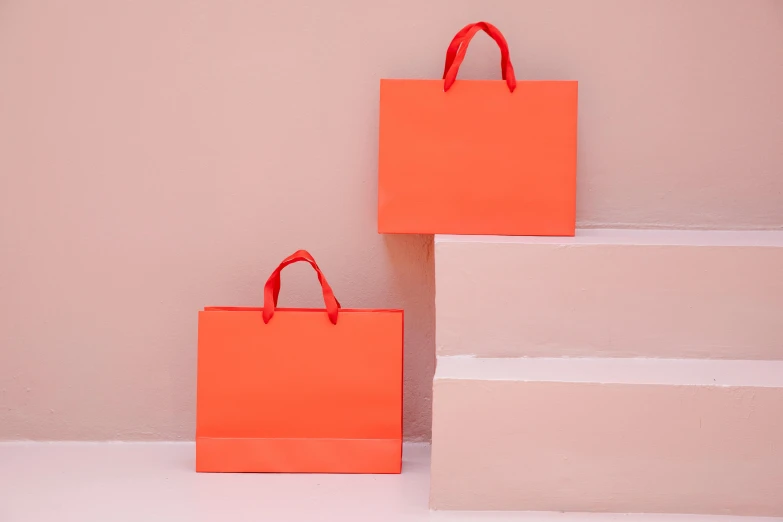 two orange shopping bags sitting next to each other, pexels contest winner, minimalism, pastel pink neon, red hue, cardstock, very large