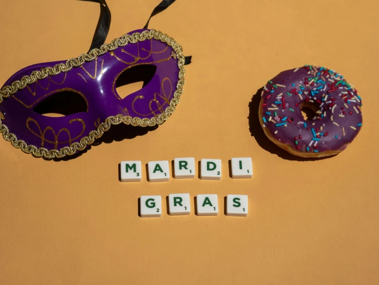 a purple mardi gras mask next to a doughnut, an album cover, trending on pexels, papyrus, background image, celebration costume, word