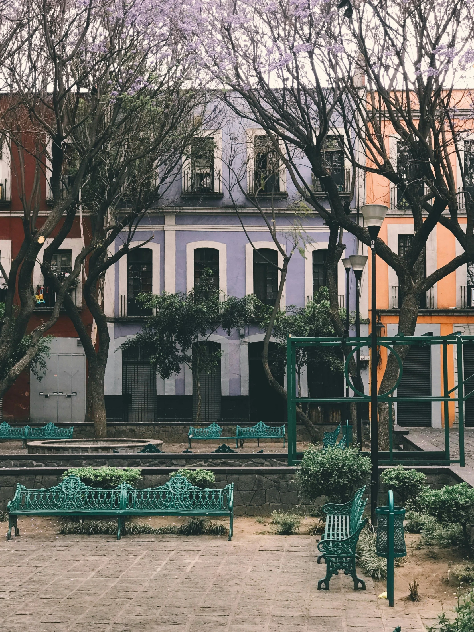 a couple of green benches sitting next to each other, a colorized photo, pexels contest winner, quito school, the neat and dense buildings, colorful otherworldly trees, moody : : wes anderson, square