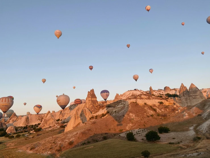 a bunch of hot air balloons flying in the sky, by irakli nadar, pexels contest winner, sheer cliffs surround the scene, cornucopia, early morning light, grayish