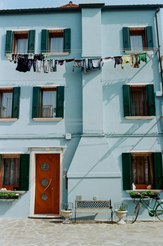 a blue building with a bicycle parked in front of it, laundry hanging, venice, sea - green and white clothes, exterior