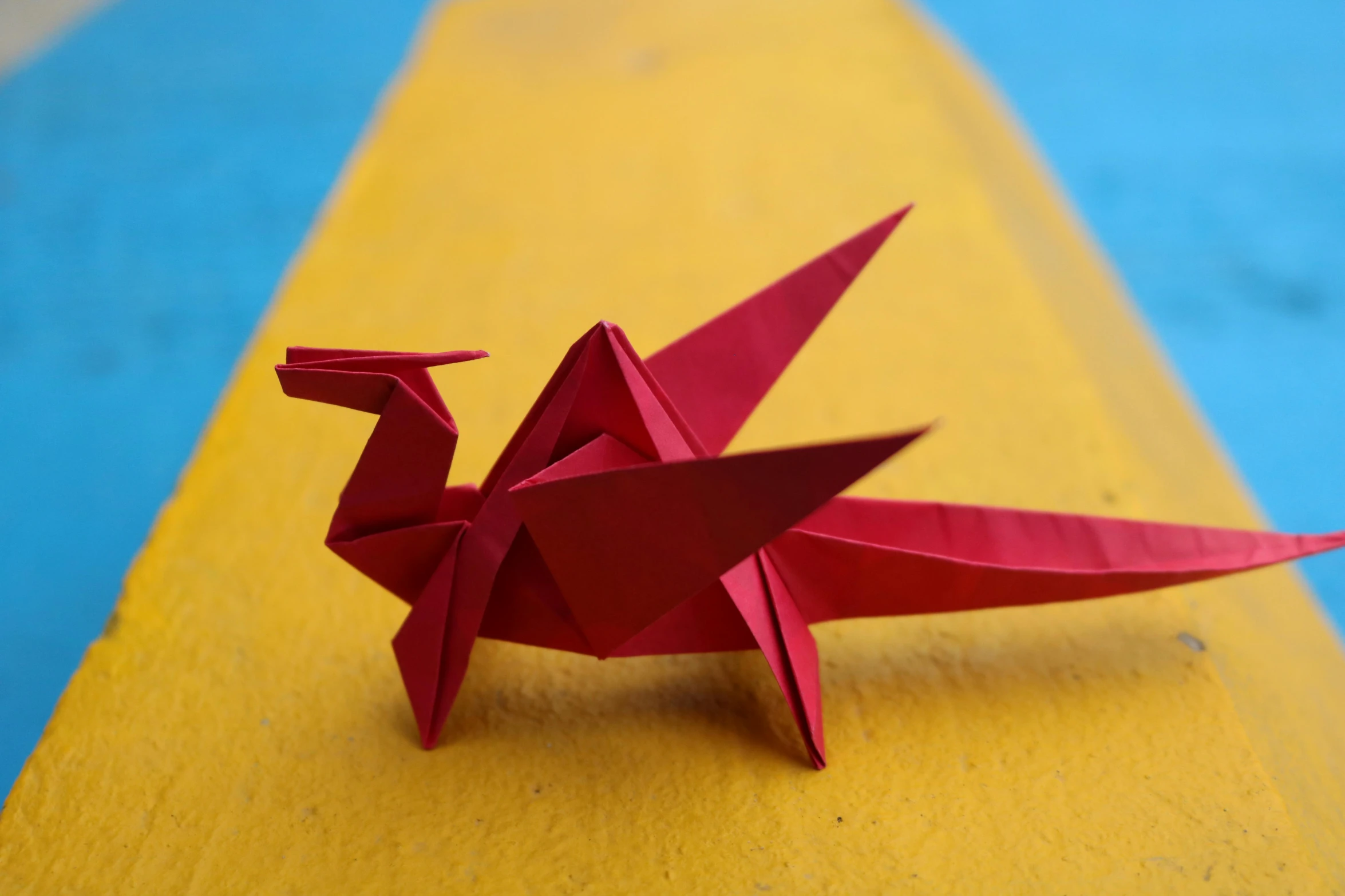 a red origami bird sitting on top of a yellow table, inspired by Uragami Gyokudō, pexels contest winner, kinetic art, sea dragon, battle pose, islamic, 2040