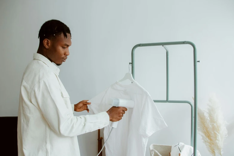 a man standing in front of a bed holding a white shirt, an airbrush painting, pexels contest winner, working clothes, man is with black skin, with electric arc device, gif