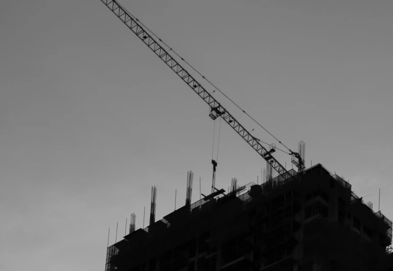 a black and white photo of a crane on top of a building, building blocks, silhouette of man, working hard, tall thin build