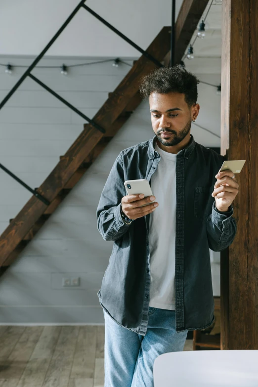 a man standing in a room looking at his cell phone, pexels contest winner, with two front pockets, holding an ace card, three quater notes, standing on a shelf