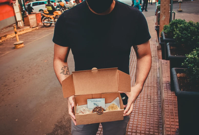 a man wearing a face mask holding a box of food, a photo, by Adam Rex, pexels contest winner, wearing shipibo tattoos, detailed product image, biker, with a wooden stuff
