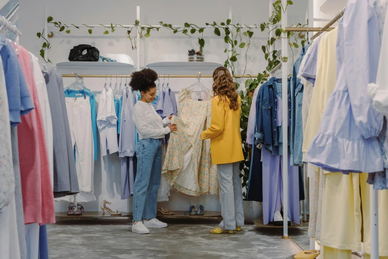 a couple of women standing in front of a rack of clothes, trending on pexels, happening, in blue and yellow clothes, inspect in inventory image, thumbnail, white clothing