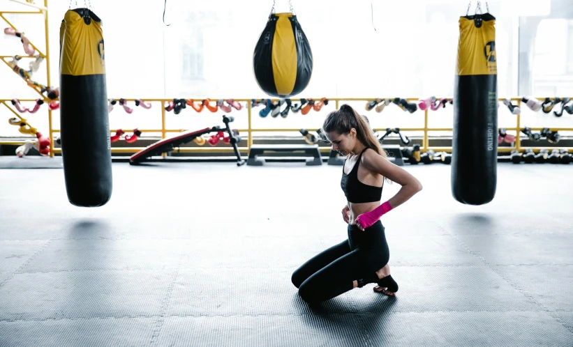 a woman squatting next to a punching bag, pexels contest winner, black and yellow tracksuit, heartbreak, thumbnail, full body picture