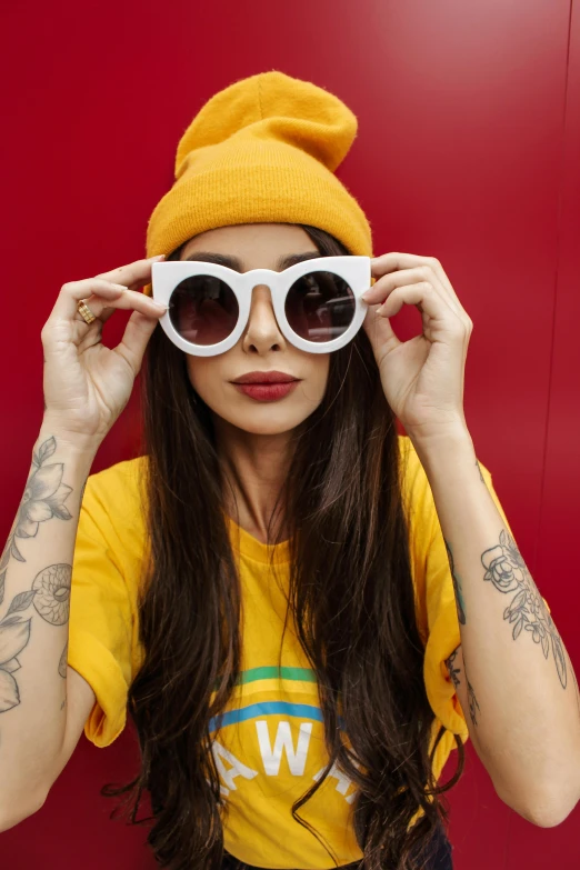 a woman wearing a yellow hat and sunglasses, inspired by Elsa Bleda, trending on pexels, pop art, with tattoos, primary colors are white, young woman with long dark hair, red color theme