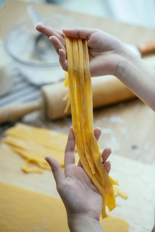 a person holding a piece of pasta in their hand, using the degrade technique, straps, creating a soft, deep