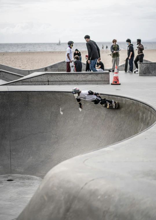 a man riding a skateboard up the side of a ramp, inspired by Seb McKinnon, concrete art, on ocean, bowl, grey, lots of people