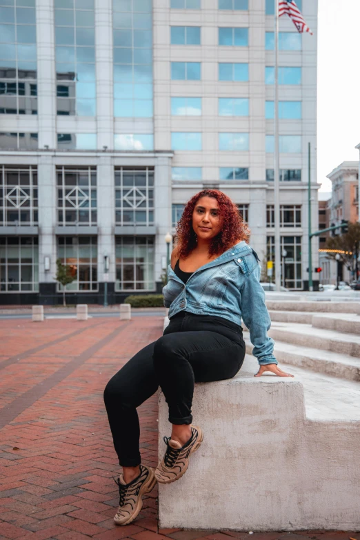 a woman sitting on a bench in front of a building, by Washington Allston, trending on pexels, renaissance, alluring plus sized model, wearing a jeans jackets, low quality photo, various posed