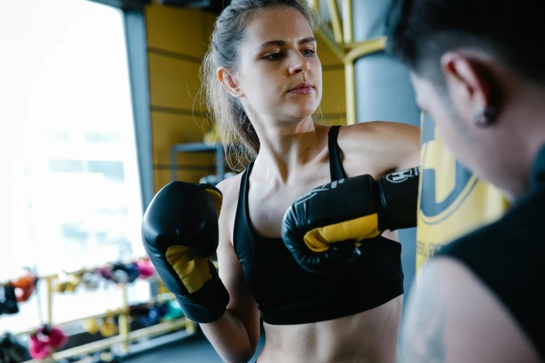 a woman standing next to a man in a gym, by Emma Andijewska, pexels contest winner, hurufiyya, punching in a bag, black and yellow tracksuit, thumbnail, no watermarks