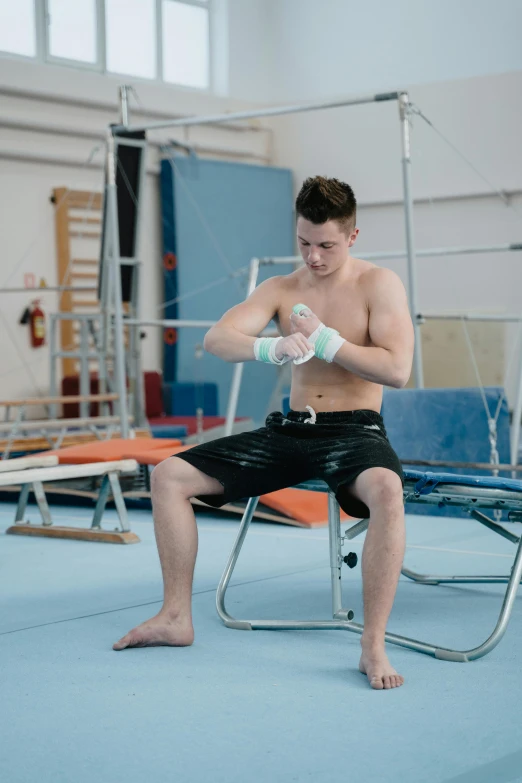 a man sitting on a trampol in a gym, by Paul Bird, happening, bandage taped fists, andrea savchenko, square, acrobat