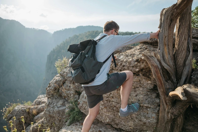 a man climbing up the side of a mountain, pexels contest winner, bag over the waist, avatar image, wearing shorts, gray