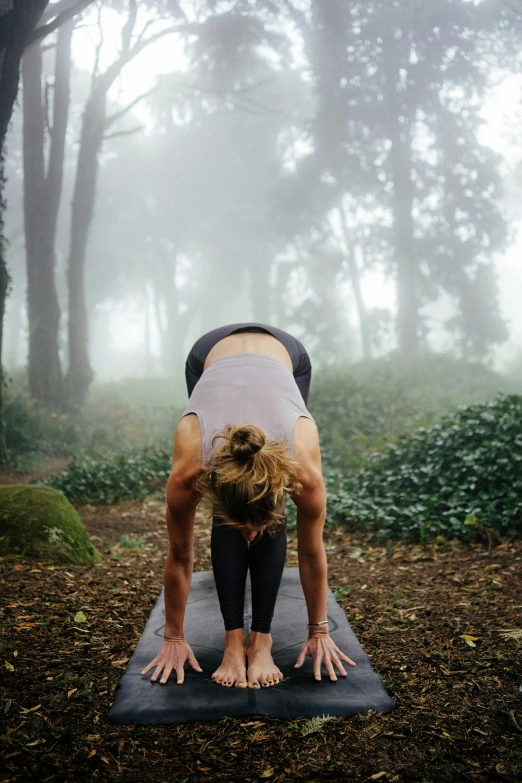 a woman doing a yoga pose on a yoga mat, by Jessie Algie, in foggy forest, crawling towards the camera, arched back, pyramid surrounded with greenery