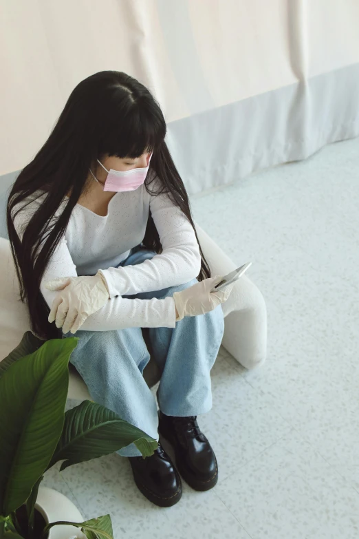 a woman sitting on the floor using a cell phone, by Jang Seung-eop, medical mask, wearing gloves, anxiety environment, next to a plant