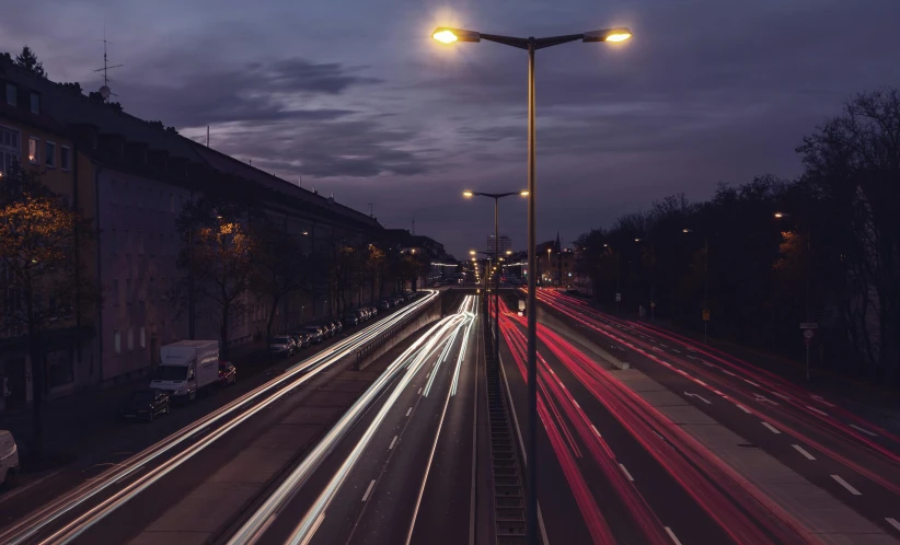 a street filled with lots of traffic next to tall buildings, by Adam Marczyński, pexels contest winner, car lights, lamp posts, freeway, light traces