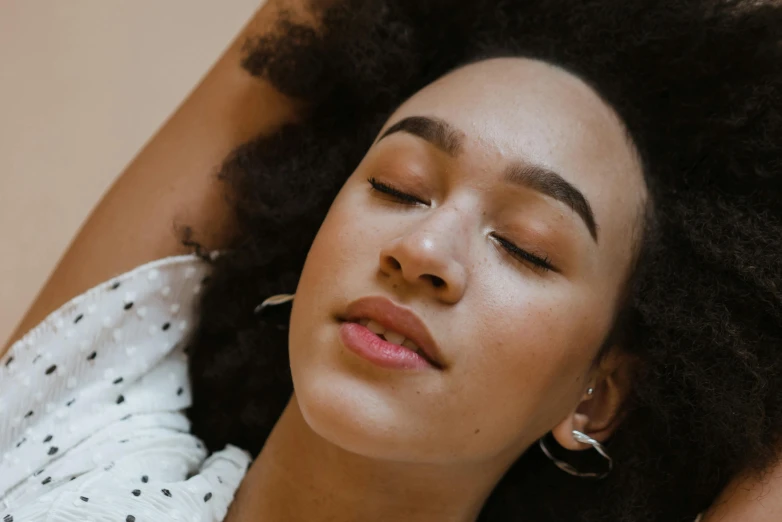 a woman laying down with her eyes closed, trending on pexels, visual art, curls on top, relaxed eyebrows, mixed-race woman, ad image