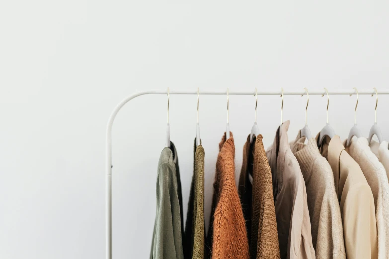 clothes hanging on a rack in front of a white wall, by Matija Jama, trending on unsplash, green and brown color palette, 🦩🪐🐞👩🏻🦳, wearing a light shirt, brown and white color scheme