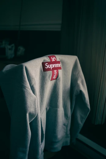 a white sweatshirt sitting on top of a window sill, happening, supreme, wearing cross on robe, label, support