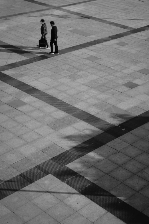 a couple of people walking across a tiled floor, postminimalism, city square, monochrome:-2, man standing, travellers