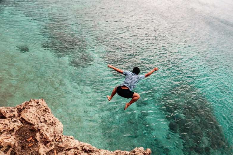 a man jumping off a cliff into the ocean, by Matija Jama, pexels contest winner, great barrier reef, cyprus, on a canva, samoan features