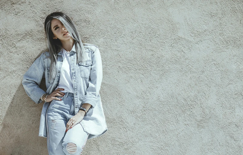 a woman leaning against a wall with her hands on her hips, trending on pexels, double denim, silver hues, background image, teenage girl