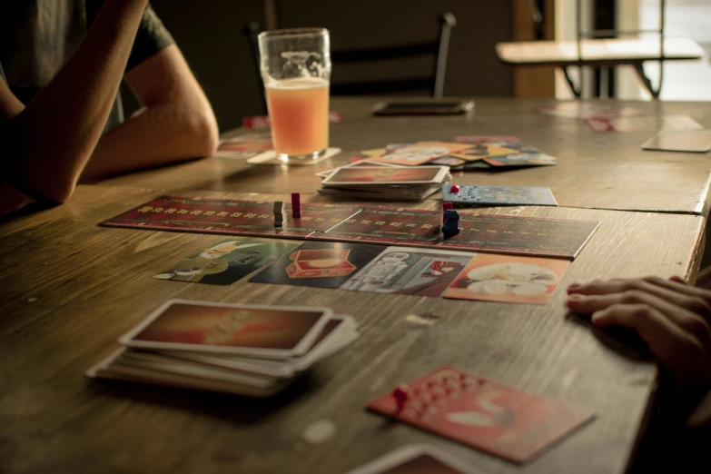 a group of people sitting around a wooden table, a picture, game level, light red and orange mood, pair of keycards on table, drinks