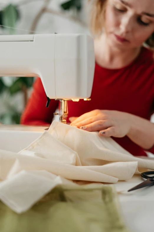 a woman is working on a sewing machine, by Nicolette Macnamara, trending on pexels, arts and crafts movement, ecru cloth, white apron, red fabric, architect